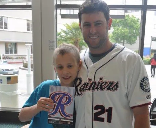 True Competitors founder Casey Coleman, in his Tacoma Rainiers jersey, smiling with a young patient in a hospital lobby