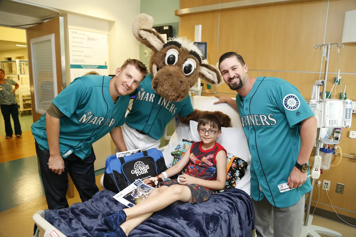 Seattle Mariners players and the Mariner Moose mascot visit a young patient in his hospital room